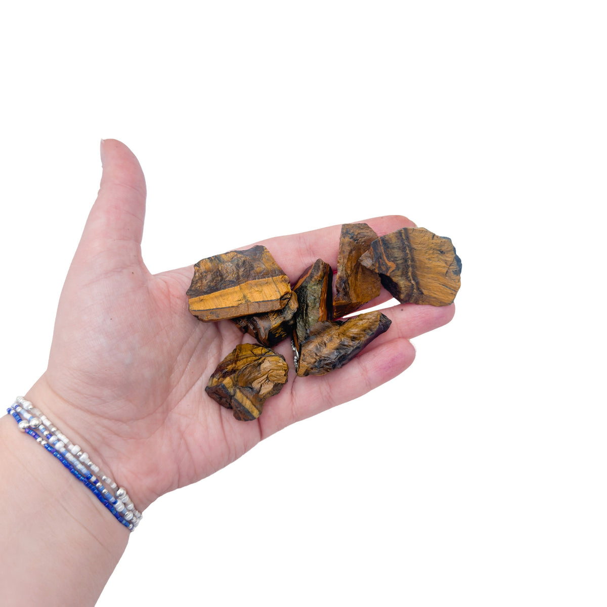 Several raw Tiger Eye stones held in an open hand for scale, showing that pieces this size sit comfortably across the palm.